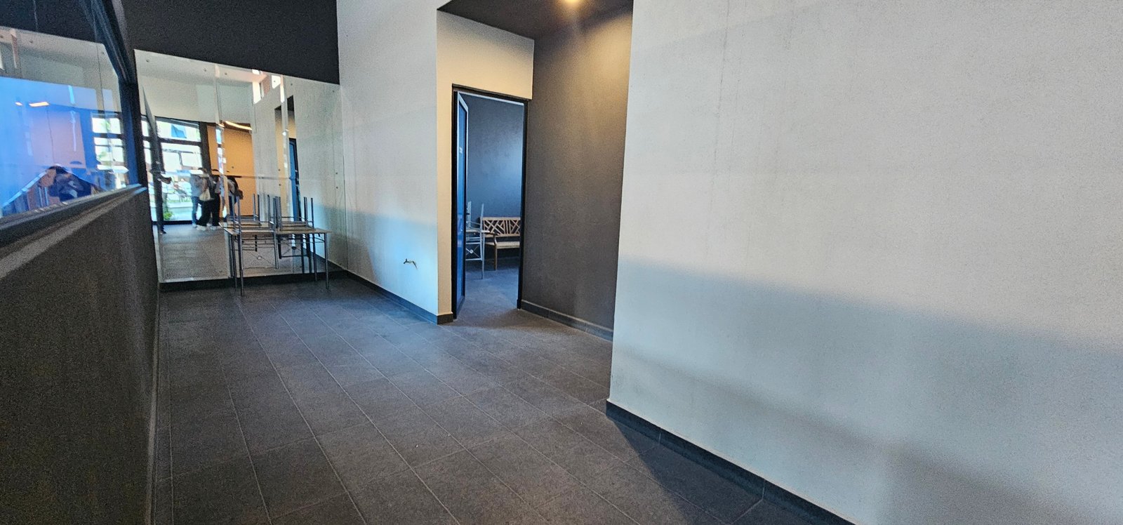 Pasillo amplio con paredes oscuras que conecta el baño del gimnasio, el gym y la alberca en Residencial Rubí, León.