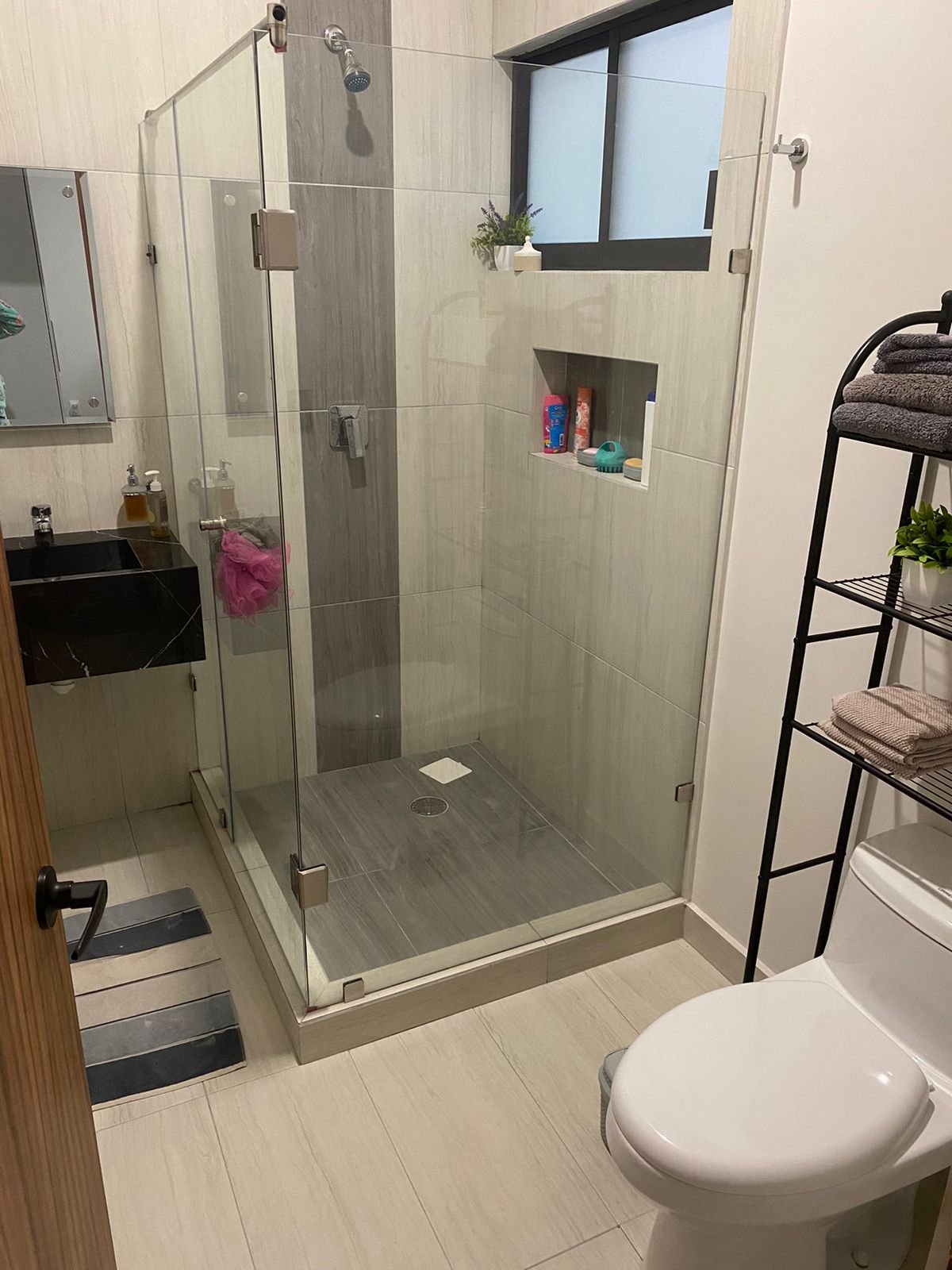 Baño moderno con ducha de cristal en departamento amueblado.